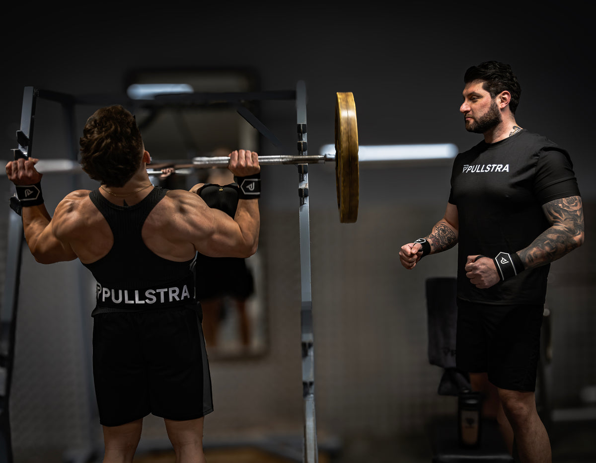 Athlète au rack de squat et coach en tenue Pullstra, avec des bandes de poignet Pullstra